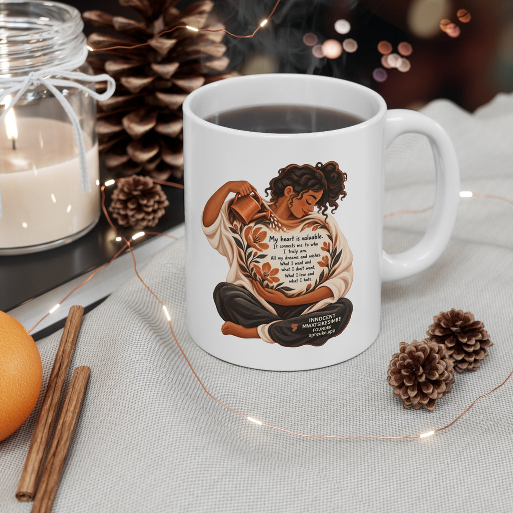 My Heart Is Valuable white ceramic mug filled with a drink, handle on the right, beside a candle, pinecones and string lights.